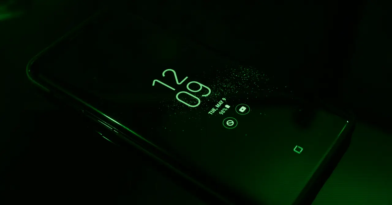 Smartphone screen lit up in the dark showing the clock and notifications, illustrating the Liquid Glass interface of OriginOS 7