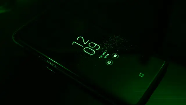 Smartphone screen lit up in the dark showing the clock and notifications, illustrating the Liquid Glass interface of OriginOS 7